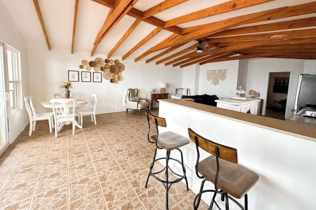 Une cuisine avec un plafond en bois, un coin repas avec des chaises blanches et un îlot central avec des tabourets.