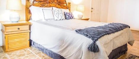 Un dormitorio con una cama grande, cabecera de madera, dos mesitas de noche y una puerta al fondo.