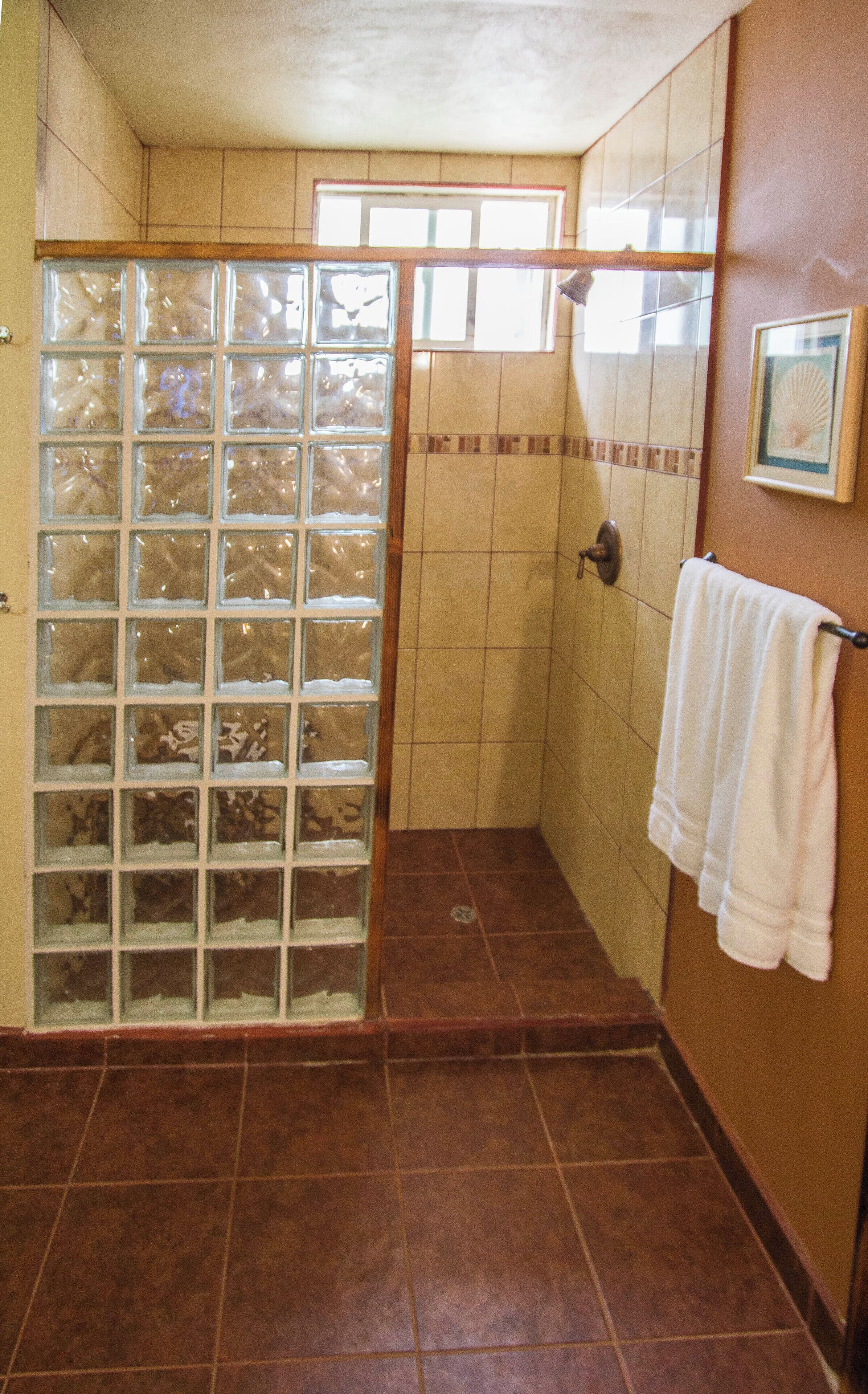 A bathroom with a shower stall, tiled walls, a towel rack, and a window.