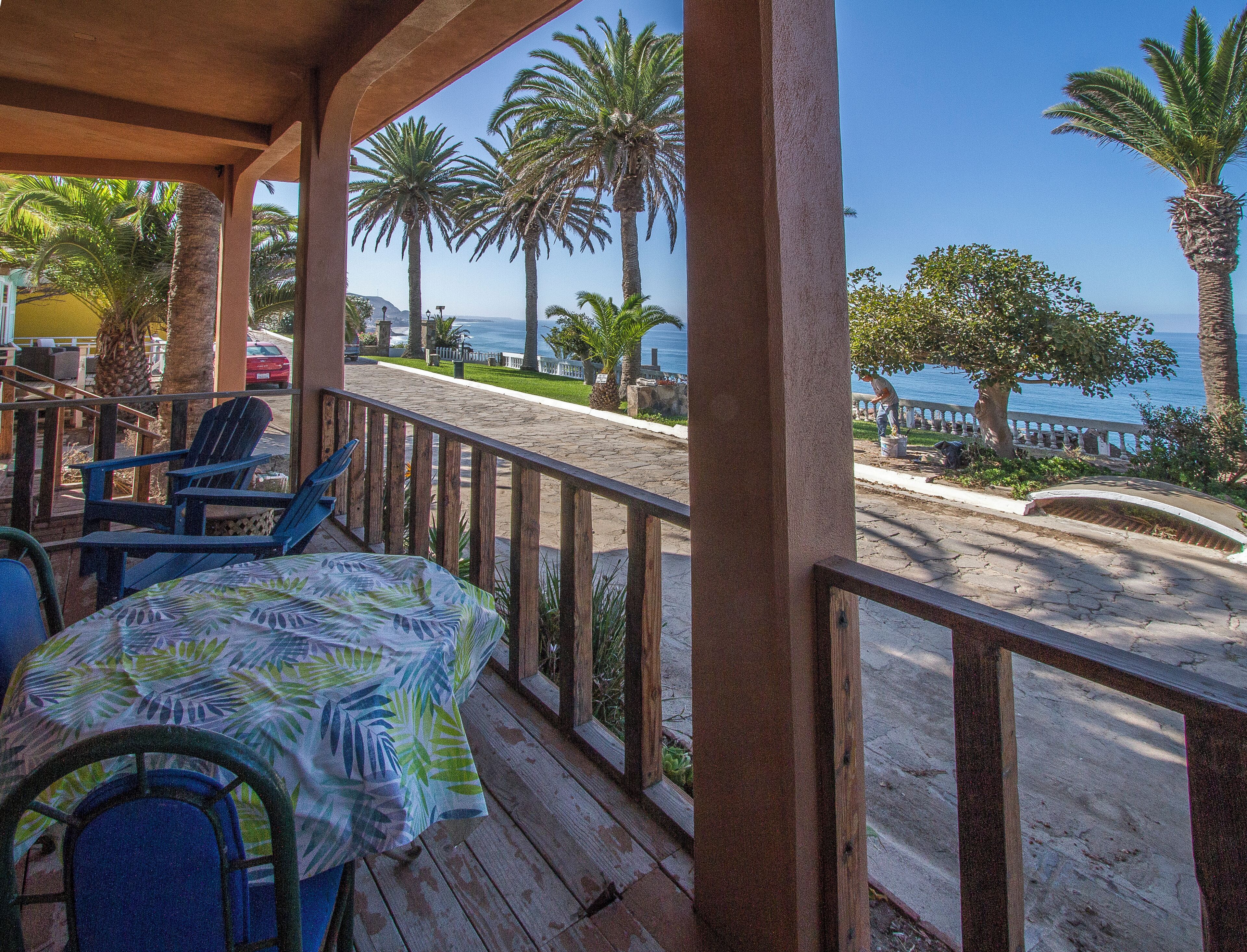 A covered outdoor seating area with a table and chairs, overlooking a sandy beach and the ocean.