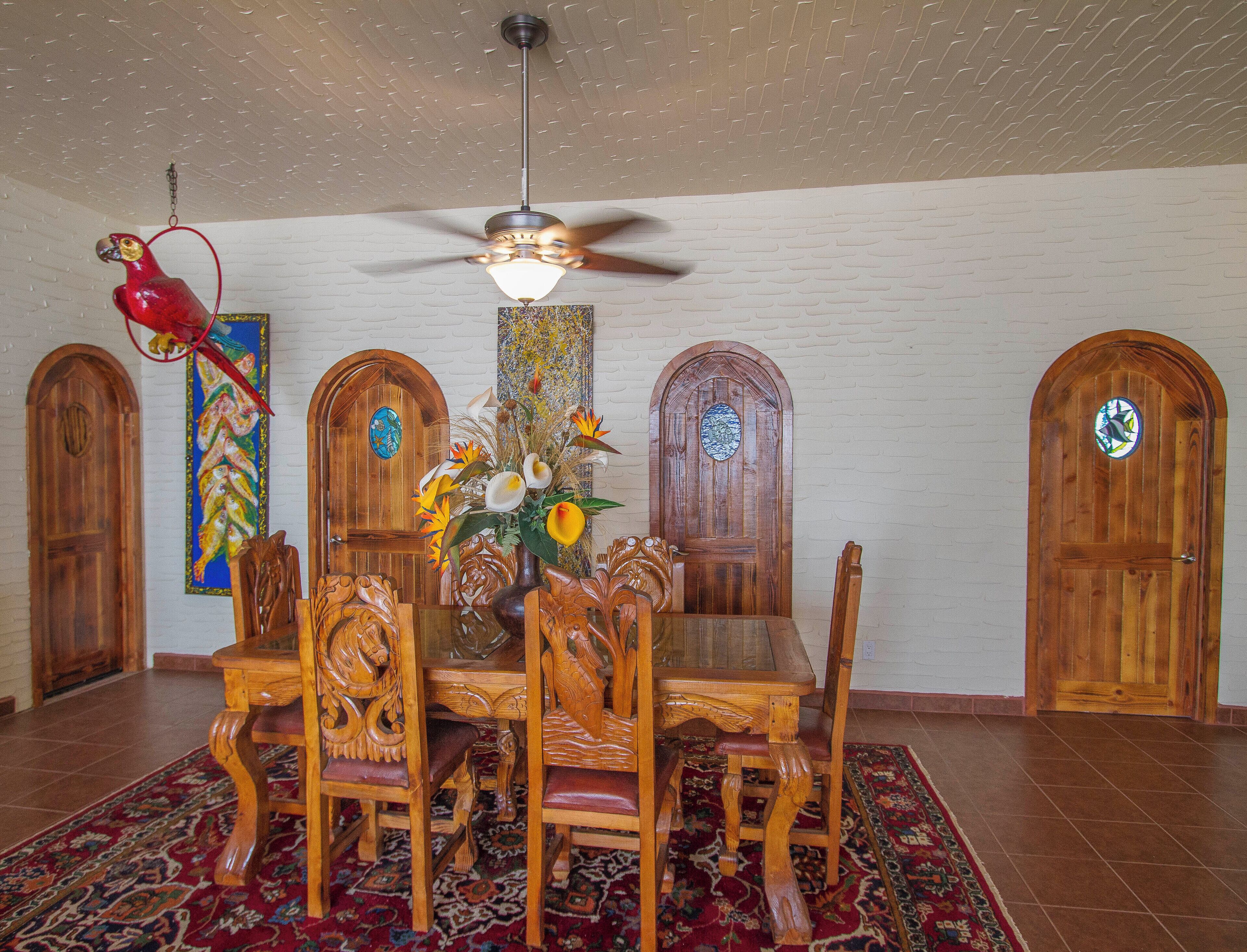 A dining area with a wooden table and chairs, a ceiling fan, and a red parrot decoration.