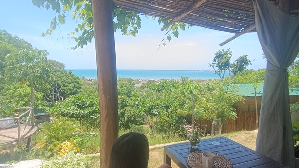 Eine Person sitzt an einem Tisch mit Blick auf eine üppige Landschaft und das Meer.
