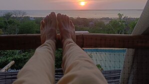 Blick auf einen Sonnenuntergang über dem Meer von einem Balkon mit Bambusgeländer.
