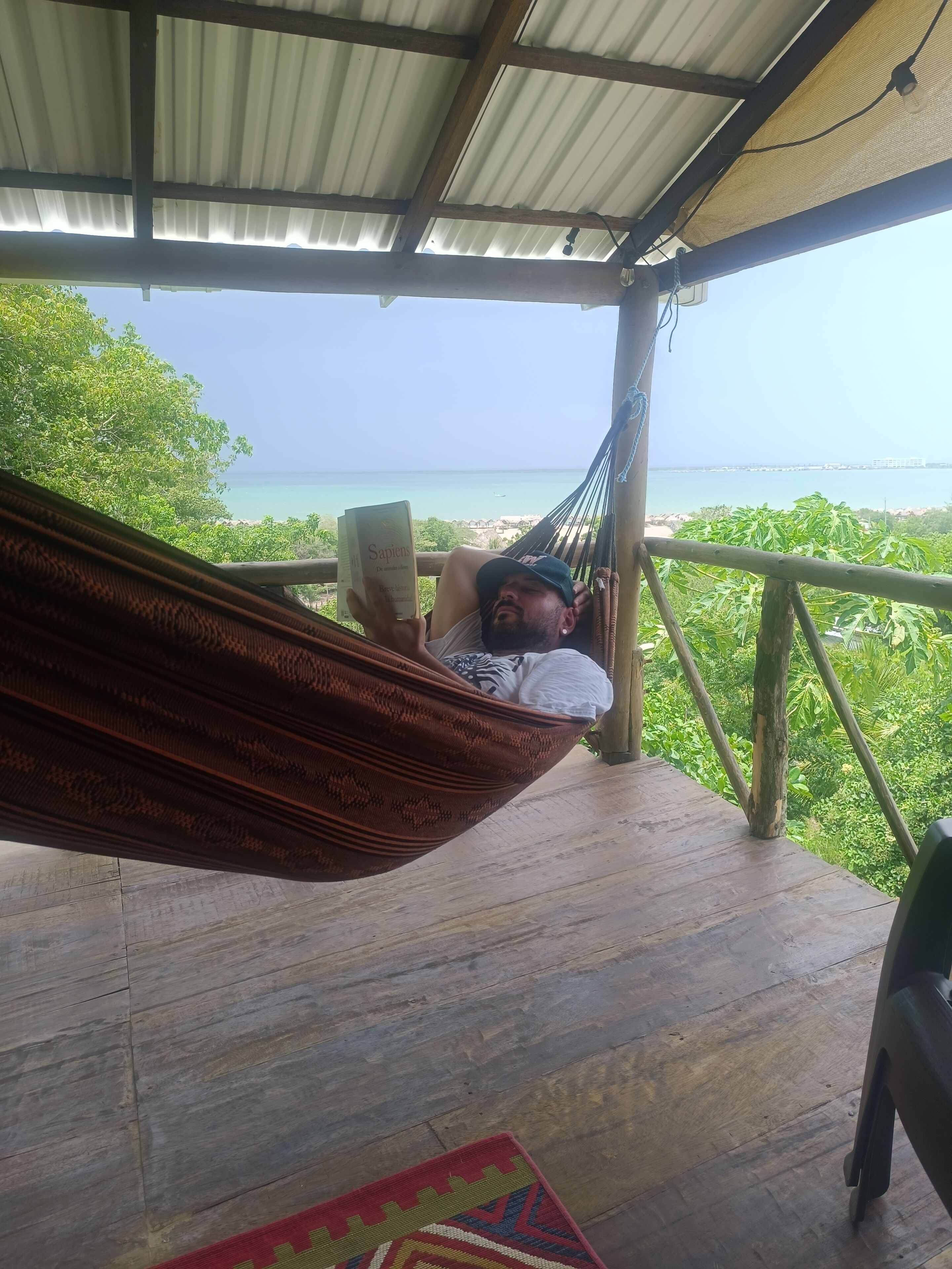 A person relaxing in a hammock on a wooden deck with a view of the ocean.