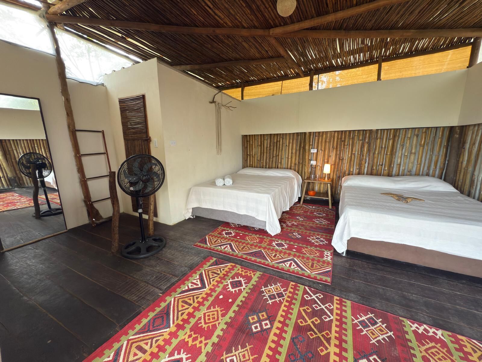 Quarto com duas camas, um ventilador, uma escada e um espelho.