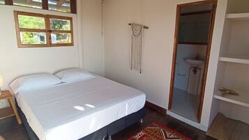A bedroom with a bed, wooden floor, a ceiling fan, a window, and a door leading to a bathroom.