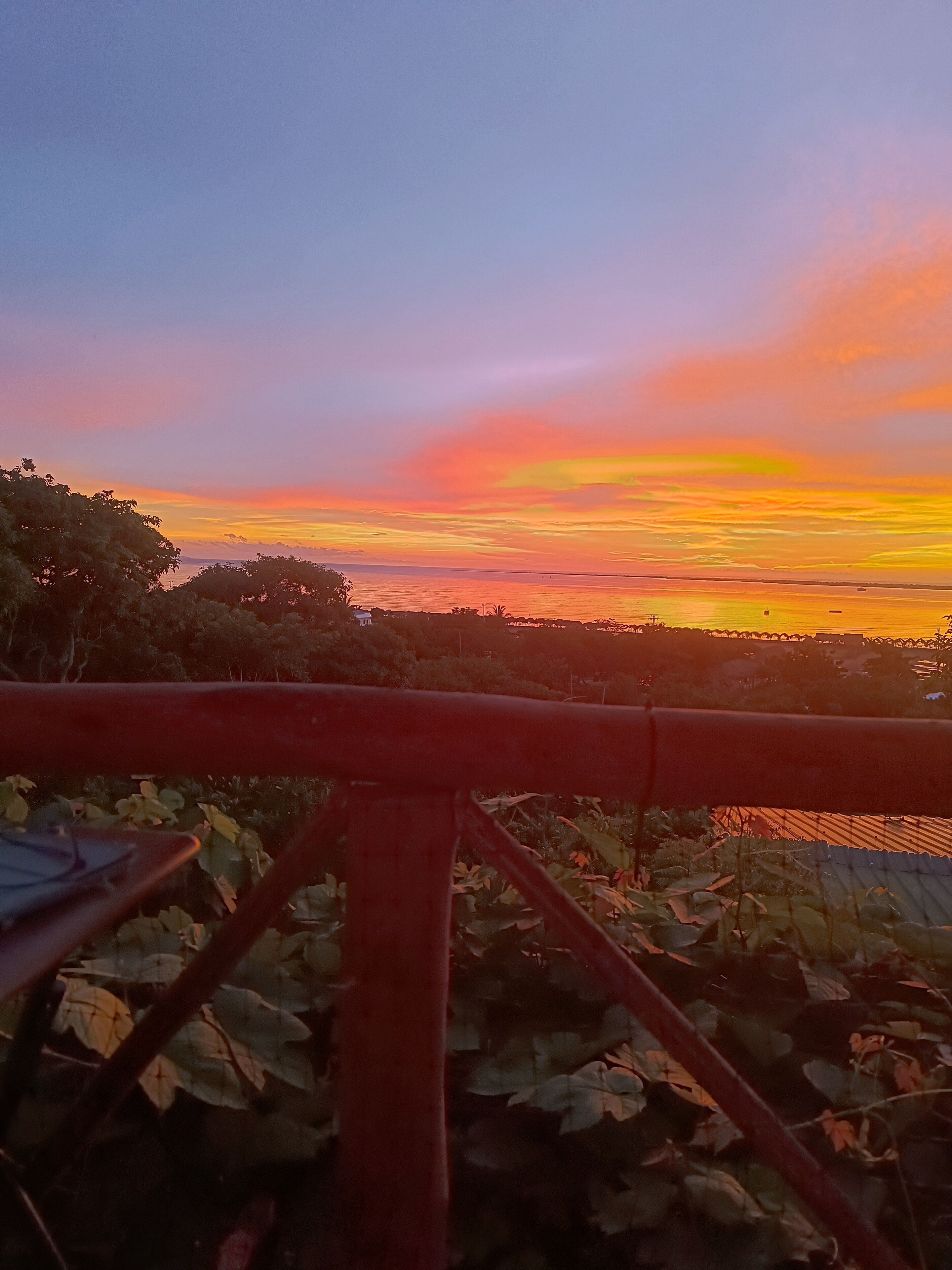 Vista do pôr do sol, com um corrimão vermelho em primeiro plano.