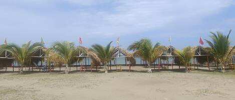 Una zona de playa con cabañas de techo de paja, palmeras y banderas.