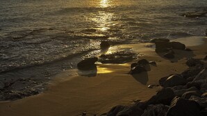 A sunset over a beach with rocks and a sailboat in the distance. - Welcome to the Dutch side of St. Maarten. 3 bedroom unforgettable ocean view. (Koolbaai)