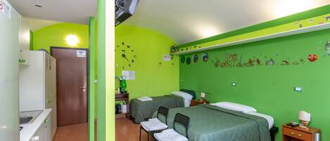 A room with a green wall, two beds, a desk, a chair, a TV, and a door.
