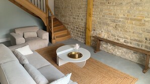 A living room with a stone wall, a wooden staircase, a grey sofa, and a white coffee table. - Exceptional group gîte for families, friends, professionals 24 pers. (Lingèvres)
