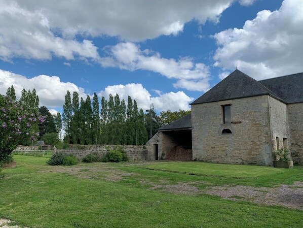 A stone building with a sloped roof, a grassy yard, and trees in the background.