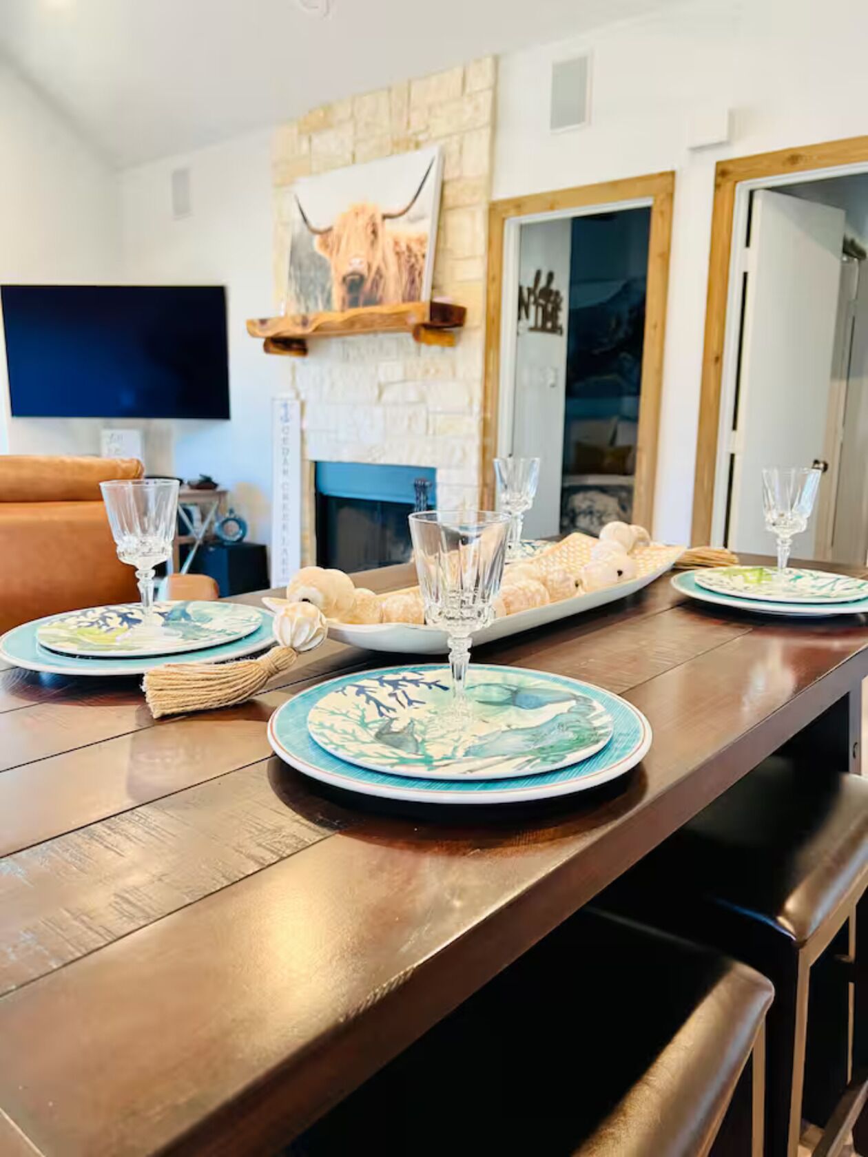 A dining table set with plates and glasses, a fireplace, a television, and a stone wall.