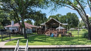 A lakeside cabin with a deck, a dock, and a grassy area with Adirondack chairs. - 
Fire Pit, Lake Views, Blackstone + Private Dock (Mabank)