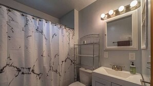 A bathroom with a white toilet, a sink with a mirror above it, and a shower curtain with a marble pattern.