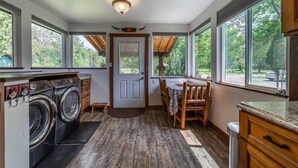A laundry room with two washing machines, a small table with chairs, and a door leading to a covered outdoor area.