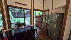 Una cocina con una mesa de comedor, sillas, un refrigerador y una ventana con vistas a la vegetación.