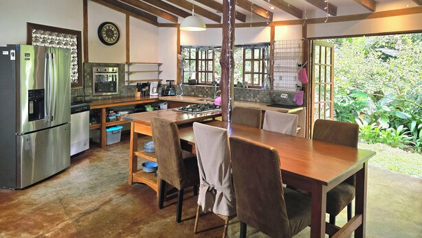 Una cocina moderna con un refrigerador de acero inoxidable, horno empotrado y comedor con mobiliario de madera.
