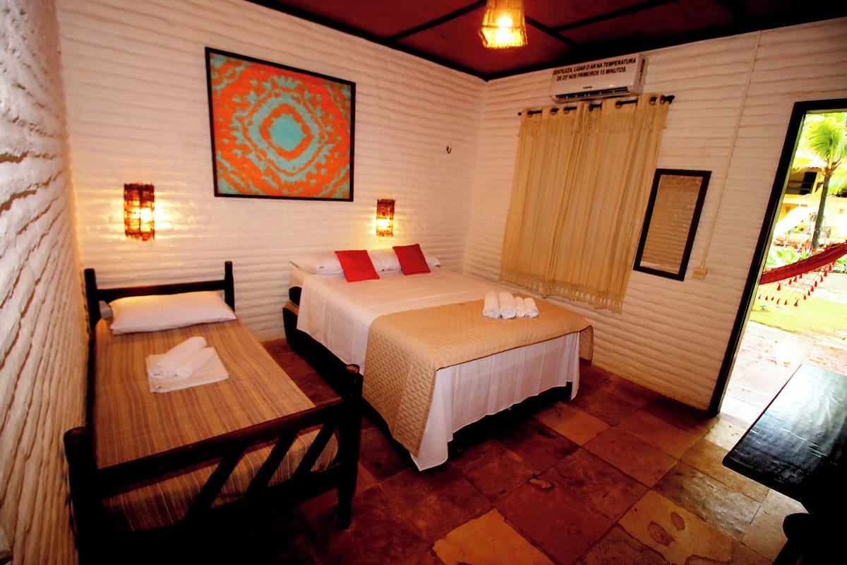Habitación con dos camas, una mesa y una silla. Cuenta con luces empotradas en la pared y una ventana con cortinas.