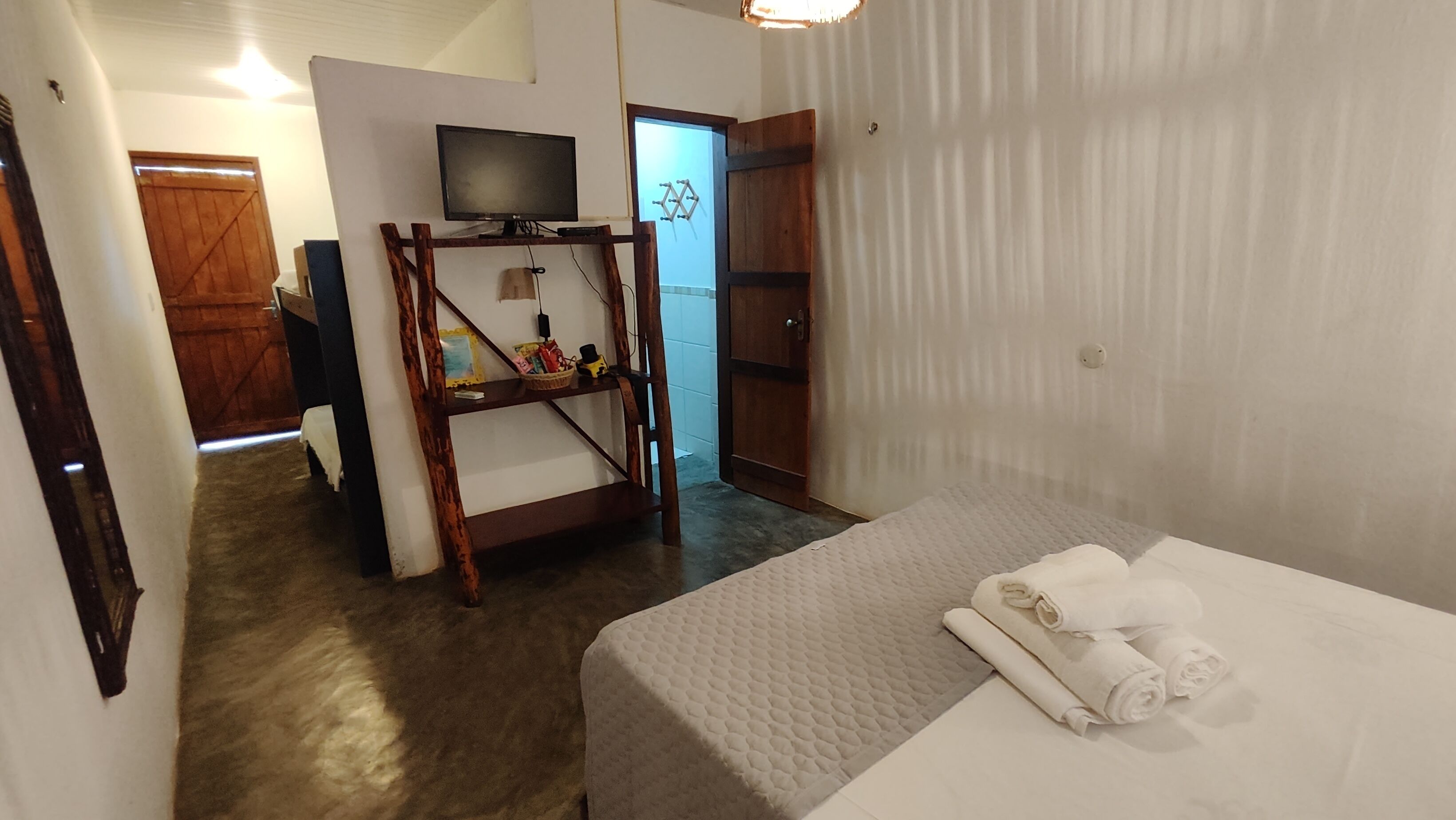 Habitación de hotel con una cama, un televisor sobre un mueble de madera, una puerta y una ventana con cortinas.
