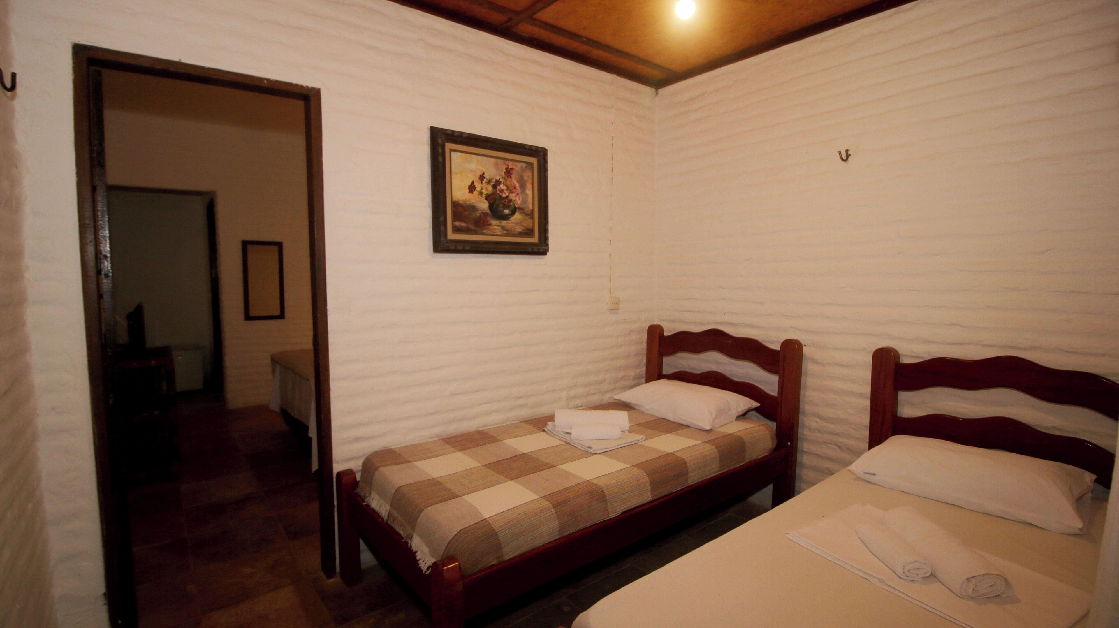A room with two wooden beds, a checkered bedspread, and a painting on the wall.