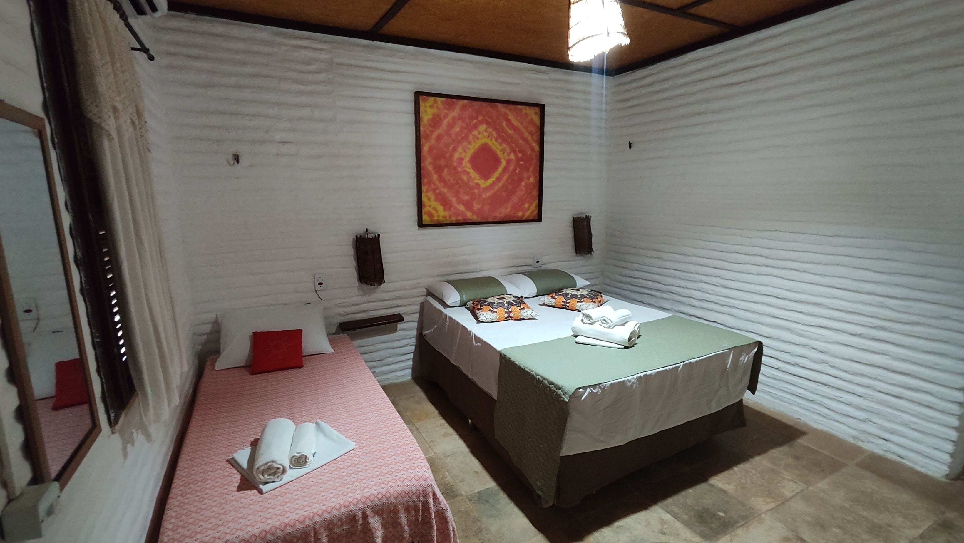 A room with two beds, a large painting on the wall, and a window with curtains.