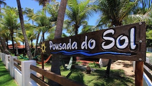 A wooden sign with the text "Pousada do Sol" surrounded by palm trees and a hammock.