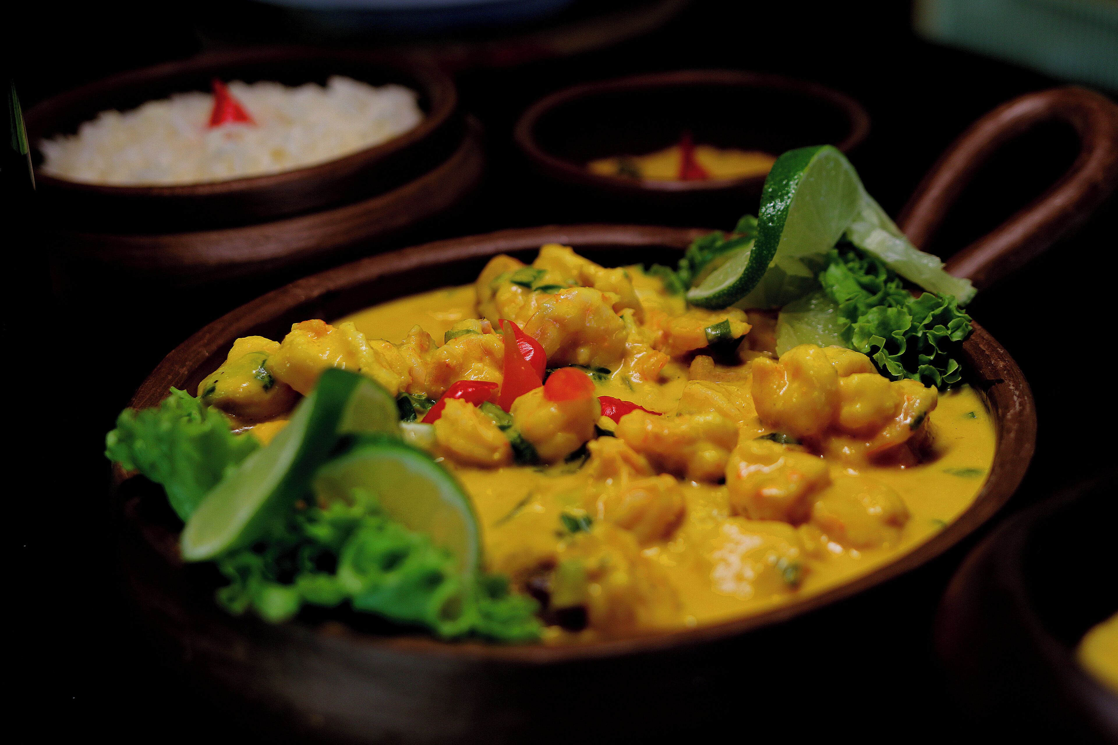 Un plato de curry amarillo con verduras y lima, servido en un tazón de madera.