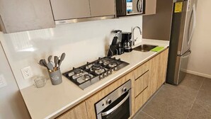 A modern kitchen with a gas stove, oven, stainless steel refrigerator, and wooden cabinets.