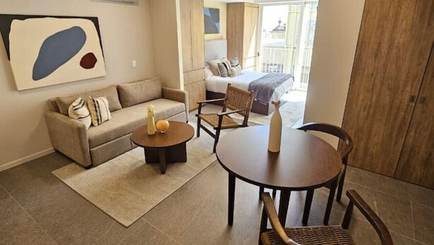 A modern living room with a sofa, a dining table with chairs, and a large abstract painting on the wall.