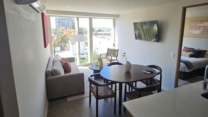 A modern kitchen with a dining area, a sofa, and a TV mounted on the wall.