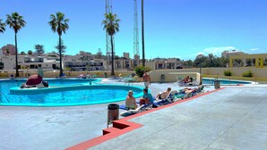 A pool area with lounge chairs and palm trees. - Ocean Panoramic View at Playa Las Americas (Playa de la Américas)