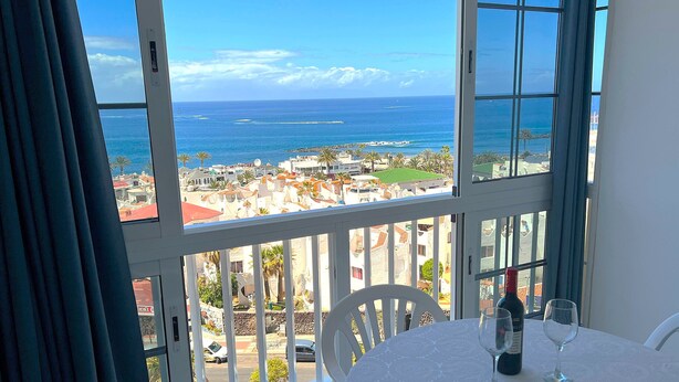 A balcony with a table set for two, overlooking a coastal town with buildings and the sea. - Ocean Panoramic View at Playa Las Americas (Playa de la Américas)