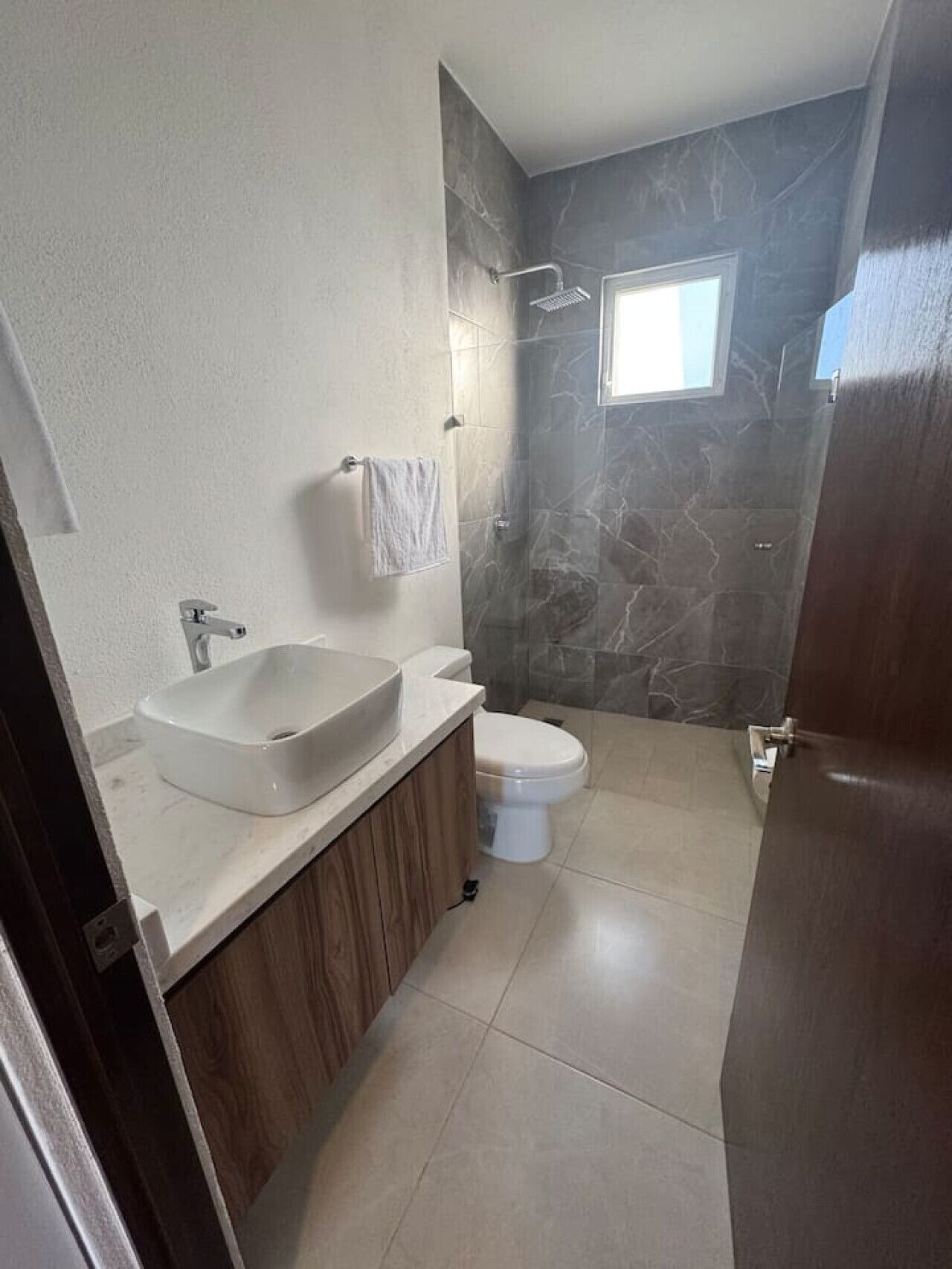 A bathroom with a large white sink, a toilet, and a shower area with a stone wall.