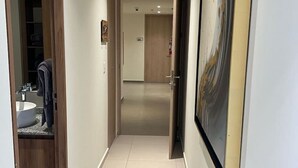 A hallway with a wooden door on the left, a bathroom with a sink and mirror, and a framed artwork on the right.