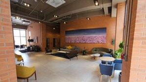 A spacious lobby with a high ceiling, exposed ductwork, and a large wall-mounted floral artwork.