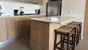 A modern kitchen with wooden cabinets, a stainless steel refrigerator, a coffee maker, and a blender on the counter.