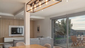 Ein modernes Wohnzimmer mit großem Fernseher, einem Holzespeisetisch und einer Glastür, die auf eine Terrasse im Freien führt.
