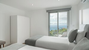 Ein modernes Schlafzimmer mit großem Fenster, einem Kleiderschrank und einem Bett mit grauer Bettwäsche.