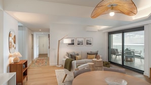 A modern living room with a sofa, a dining table, and a view of the sea through large windows. - With pool and sea view - Acqua Residence III (Funchal)