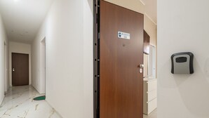 Um corredor com porta de madeira identificada como "San Benedetto Home", um tapete verde para animais de estimação e uma lixeira fixada na parede.
