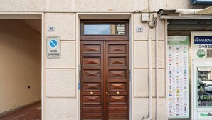 Entrada de um edifício com porta dupla de madeira, uma placa 'Passeo Carrabile' e uma placa de farmácia com lista de preços.
