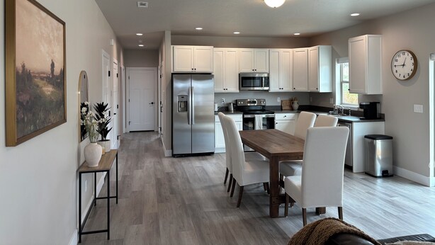 A modern kitchen with white cabinets, stainless steel appliances, and a wooden dining table. - Charming 2-bedroom house in Stevensville with AC, WiFi (Stevensville)