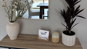 A wooden console table with a white vase of flowers, a potted plant, a WiFi sign, and a candle. - Charming 2-bedroom house in Stevensville with AC, WiFi (Stevensville)