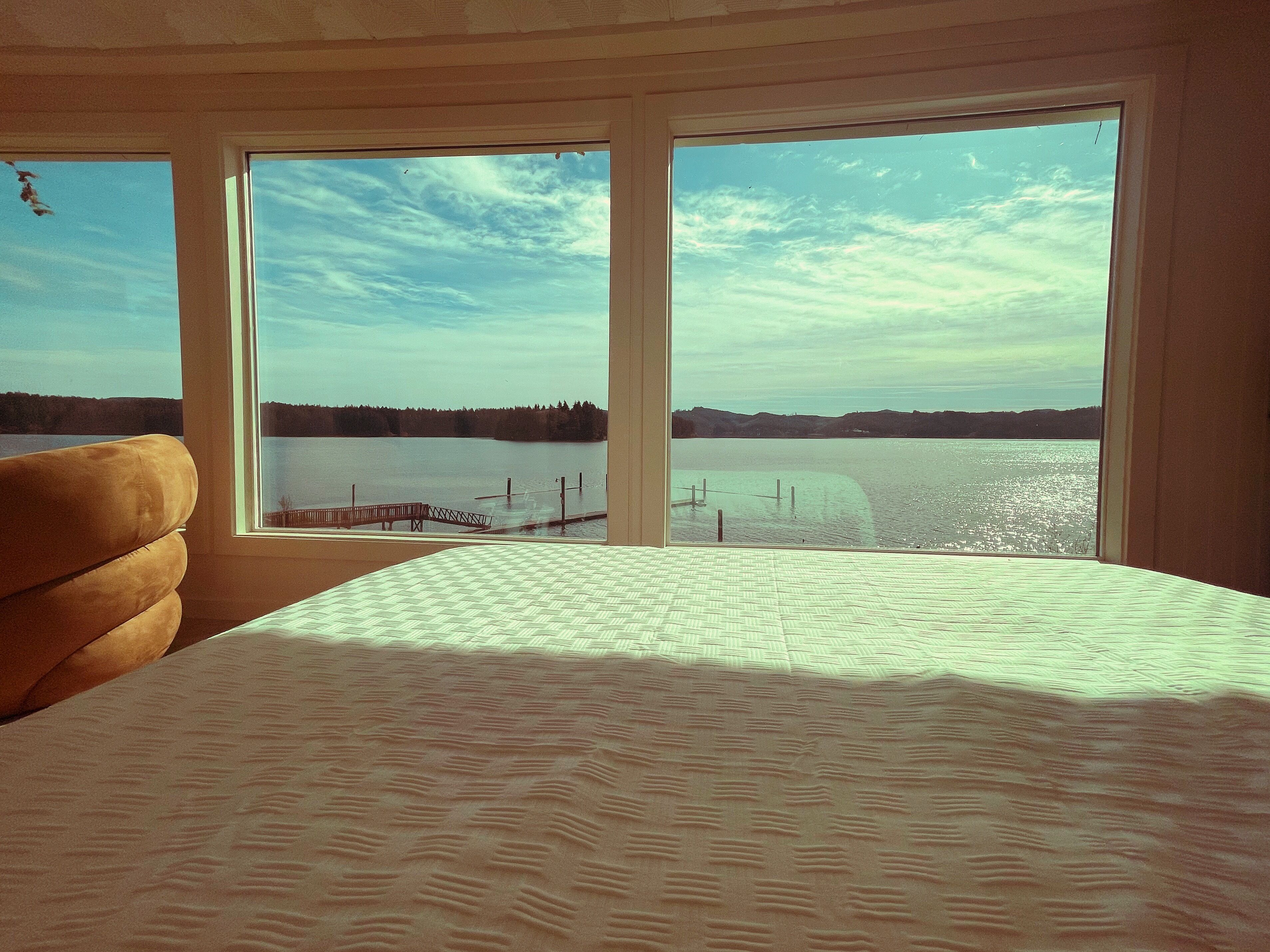 A bedroom with a large window offering a view of a lake and dock.