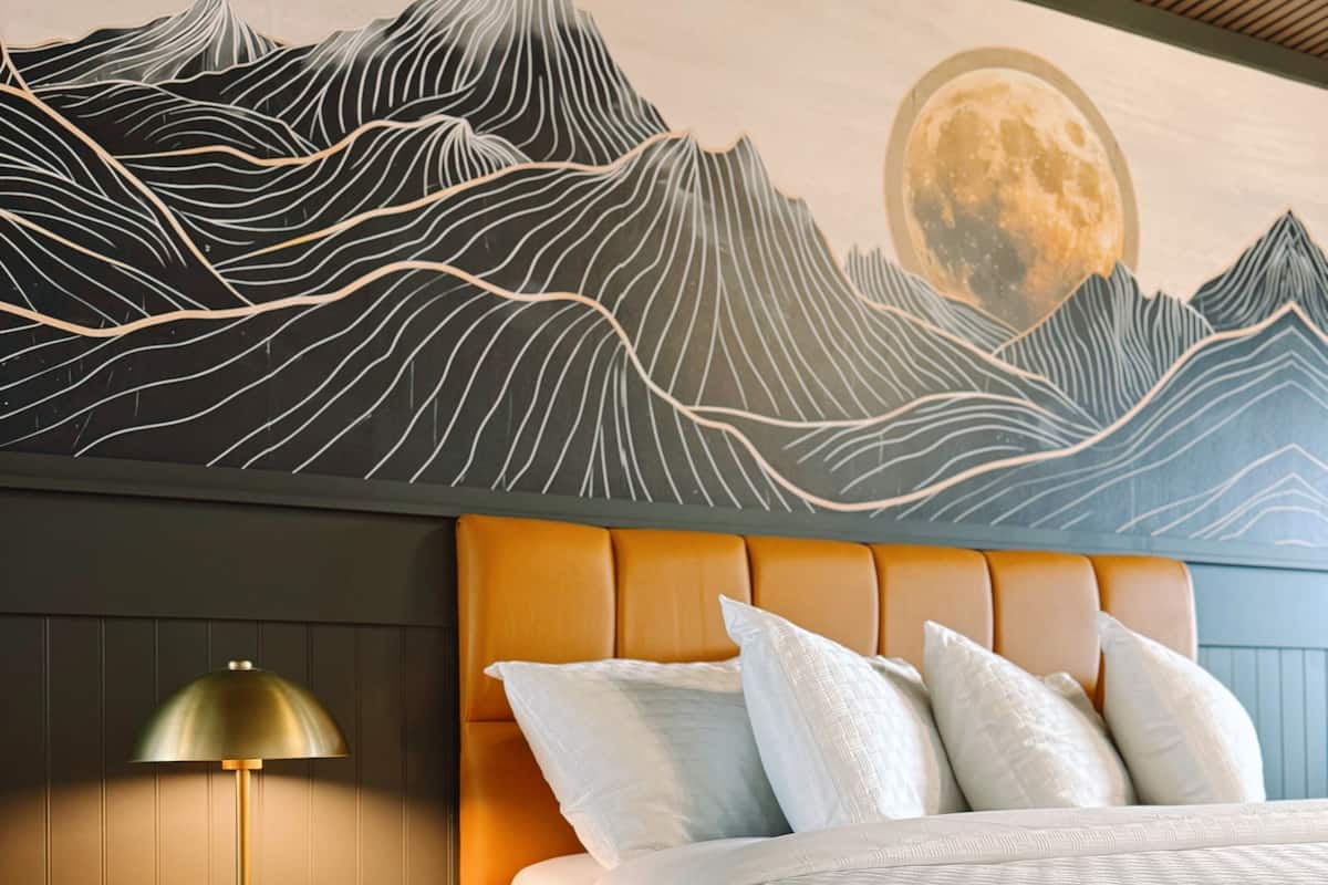 A bedroom with a bed, nightstands, a lamp, and a wall mural of mountains and a moon.