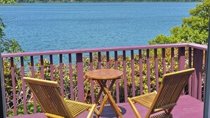 A wooden deck with two chairs and a small table, overlooking a lake with a forested shoreline. - The Florentine Waterfront Hotel (Dunes City)