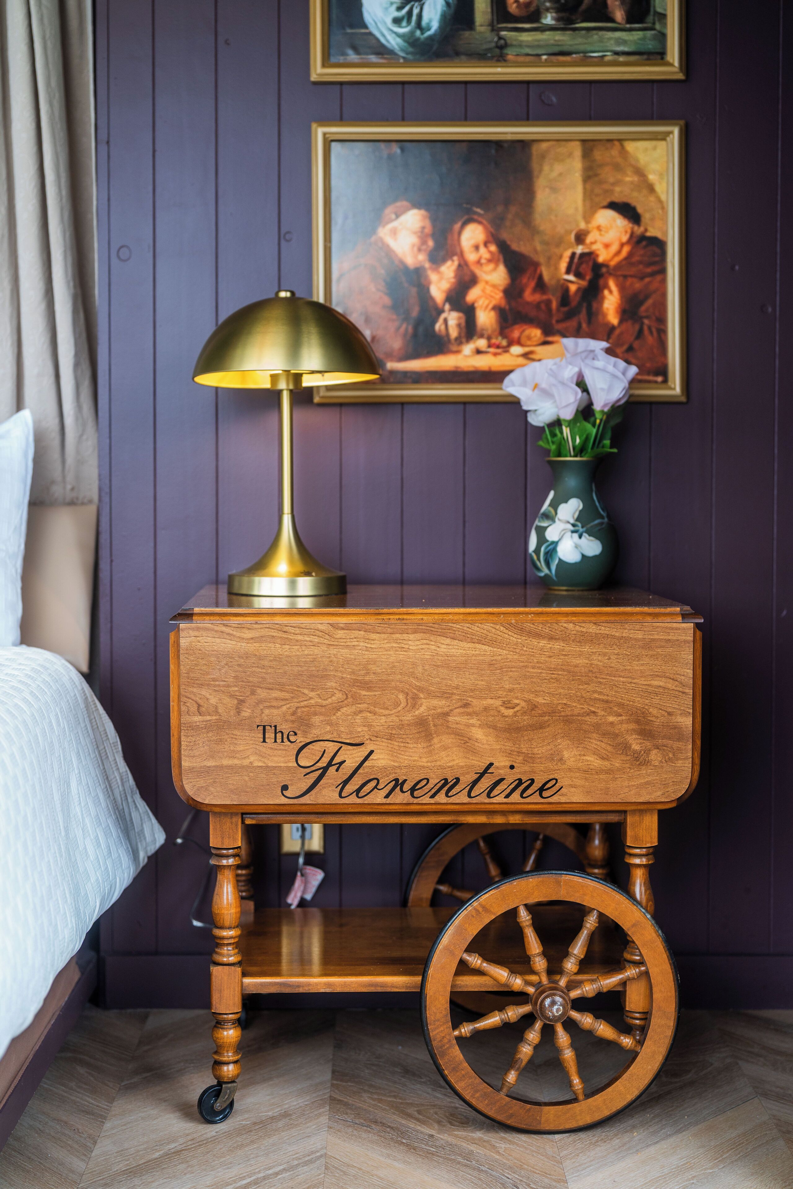A wooden nightstand with a brass lamp and a vase of flowers.