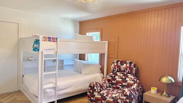 A bunk bed with a lantern, a patterned armchair, a bedside table with a lamp, and a window with a view.