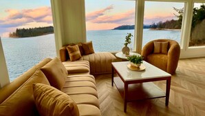 A living room with a large window overlooking a body of water and a sunset. - The Florentine Waterfront Hotel (Dunes City)